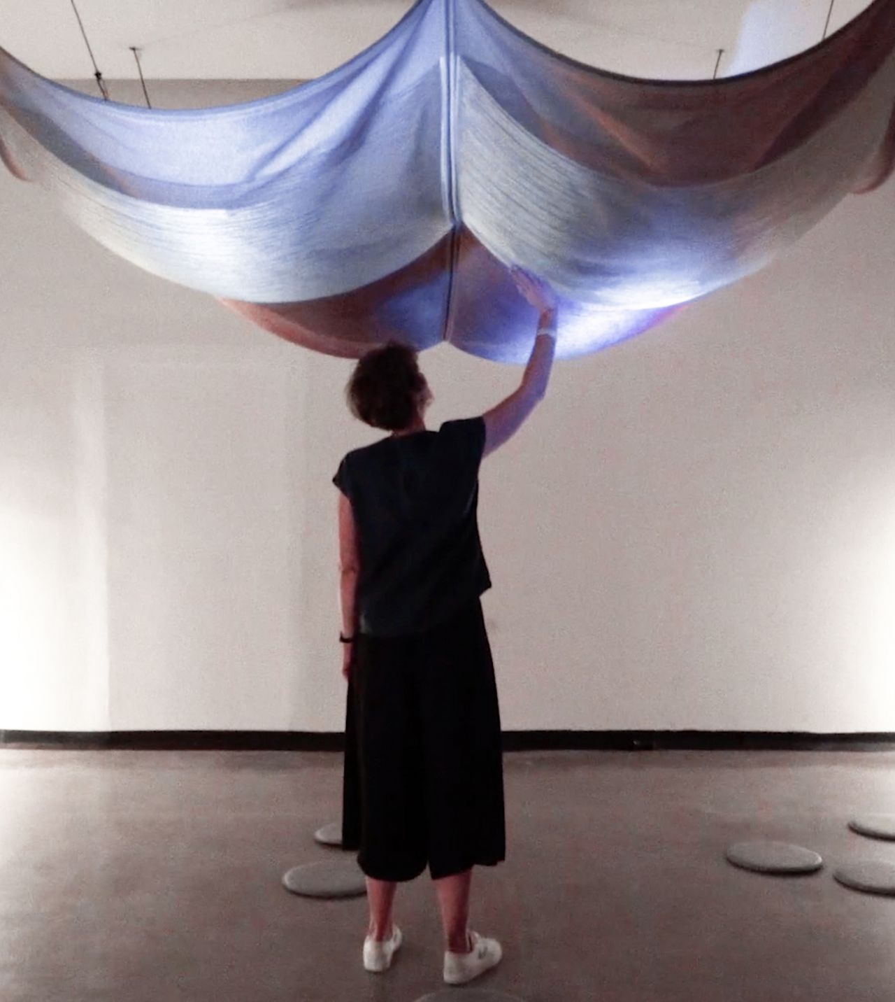 A person standing in a room touching floating fabric on the ceiling