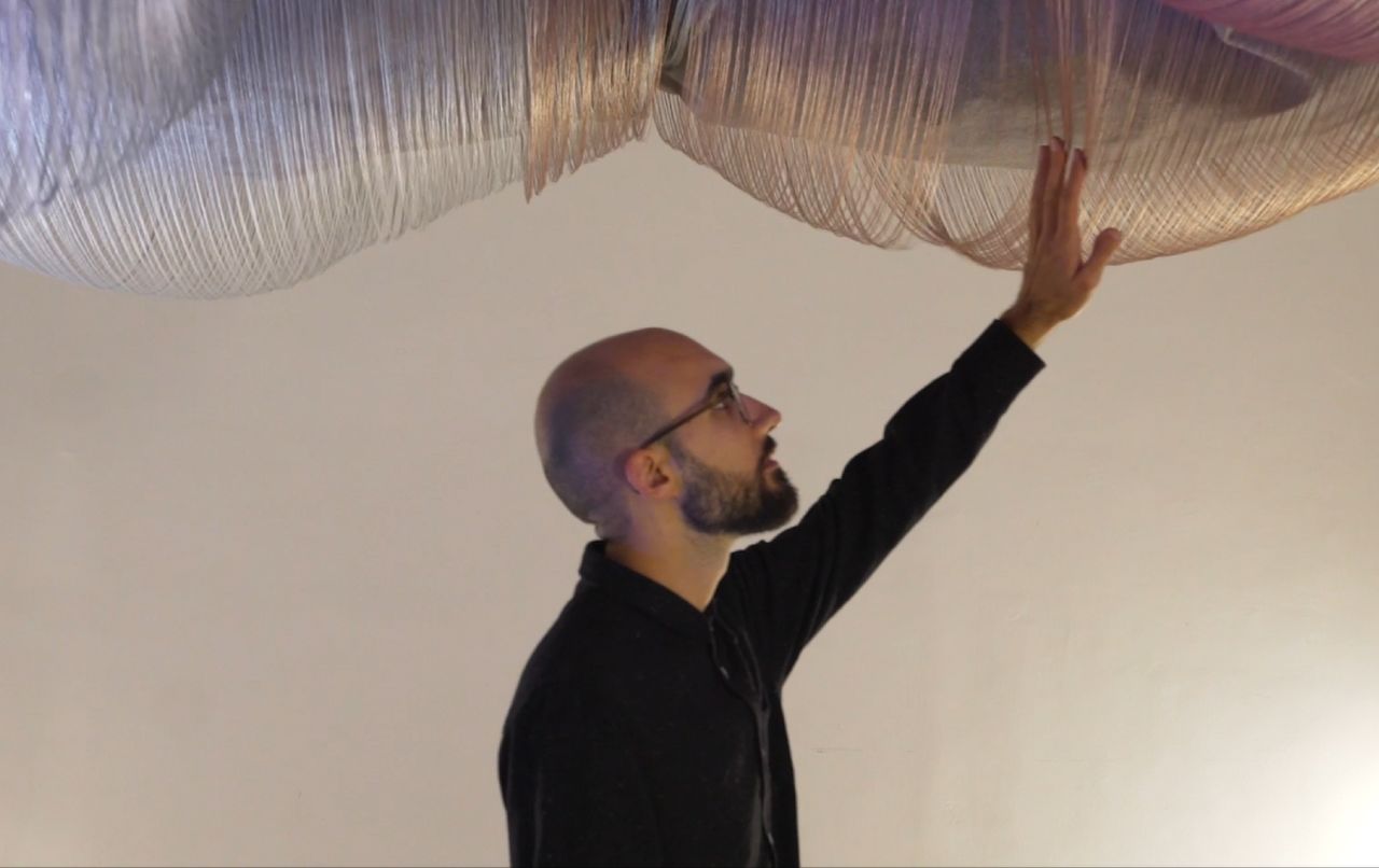 A person touching the loose threts hanging out of the woven textile on the ceiling