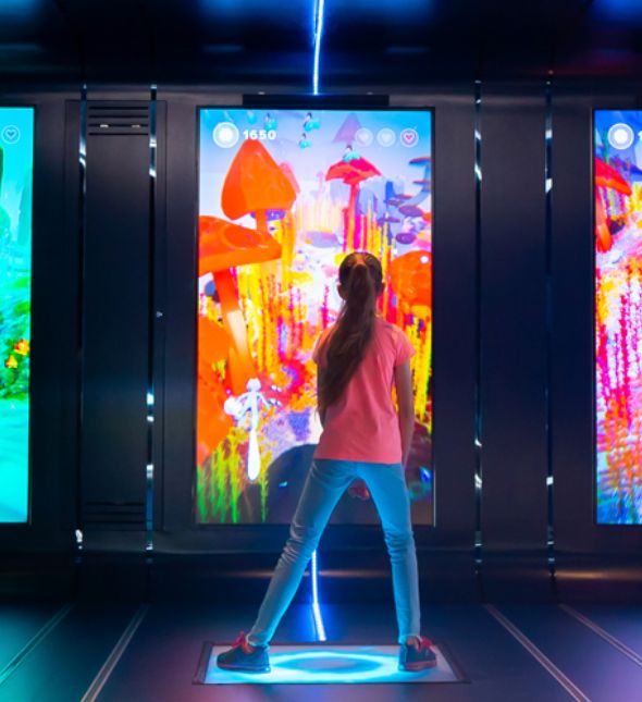A photo of a girl standing on a squre balance board. In front of her a Portrait Screen with a colorful underwater game environment.